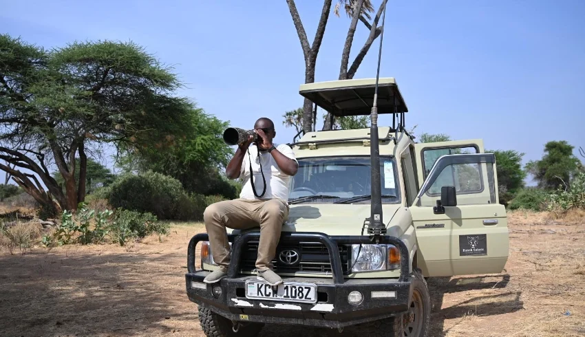 Tourist taking a photo while seated on top of a tour van - Banok Safaris ltd